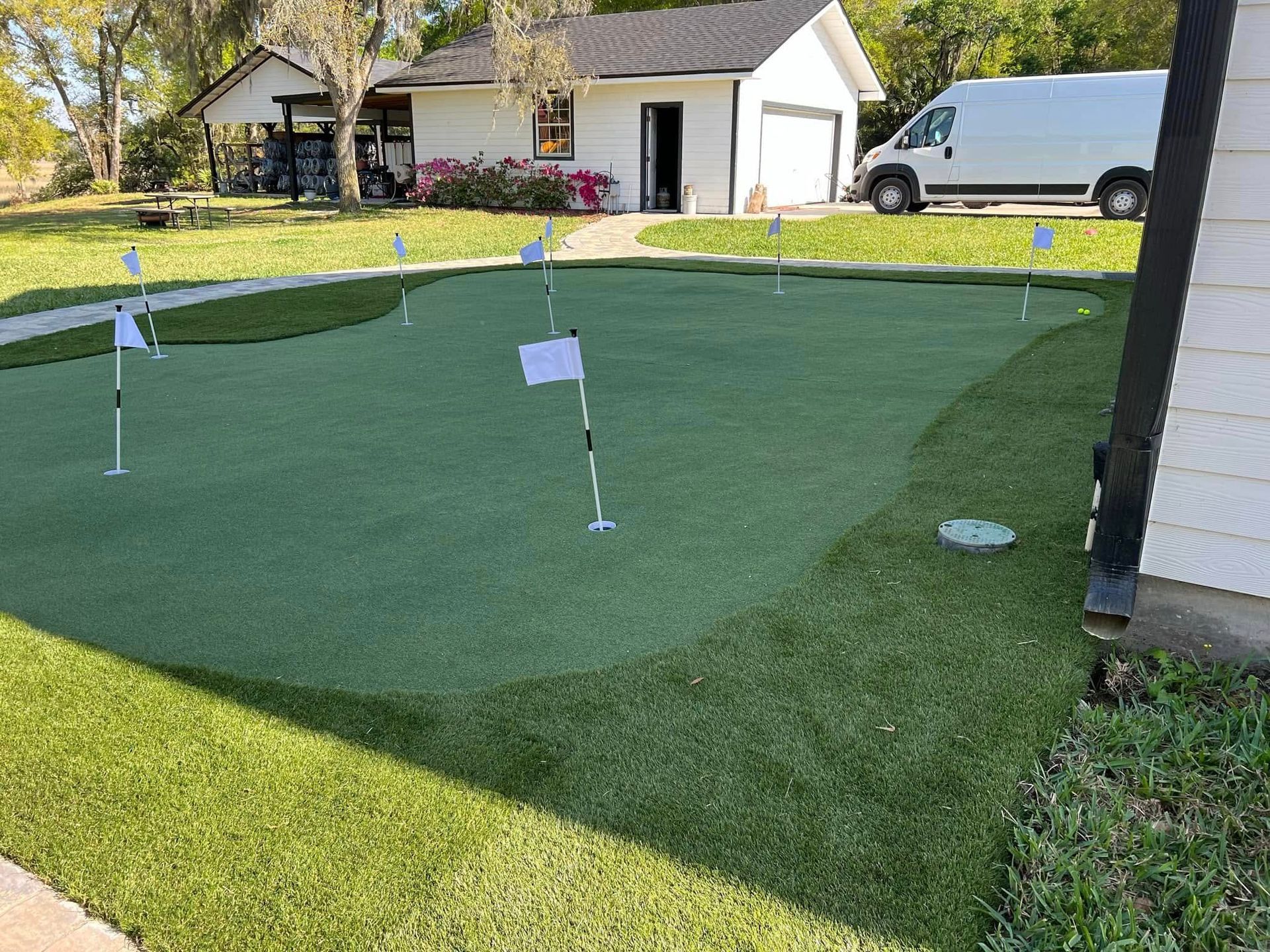 A putting green in front of a house with a white van parked in the driveway.