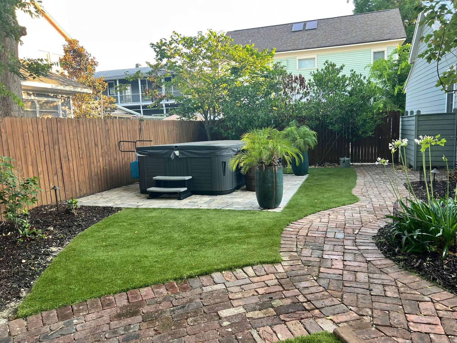 A backyard with a hot tub and a brick walkway.