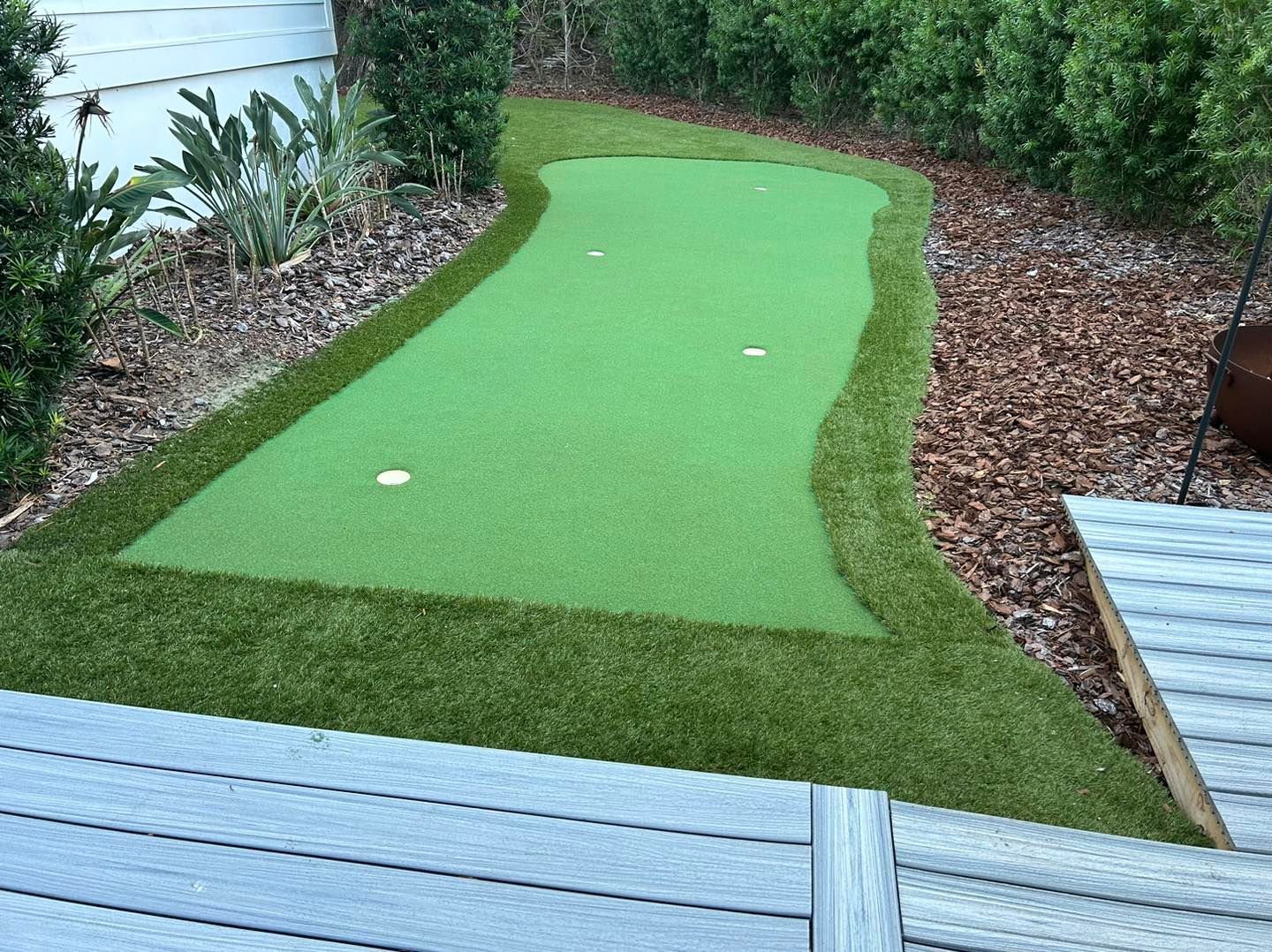 A small putting green in a backyard next to a deck.