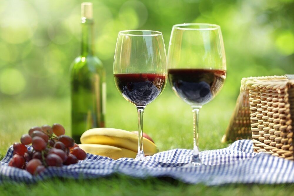 Two Glasses Of Red Wine, A Bottle Of Wine, Grapes, And A Basket On A Picnic Blanket — Café and Restaurant in Whitsundays, QLD