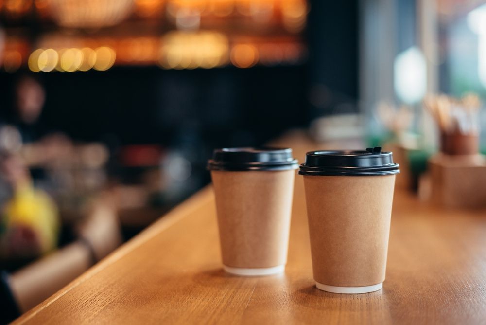 Two Paper Cups Of Coffee Are Sitting On A Wooden Table — Café and Restaurant in Whitsundays, QLD