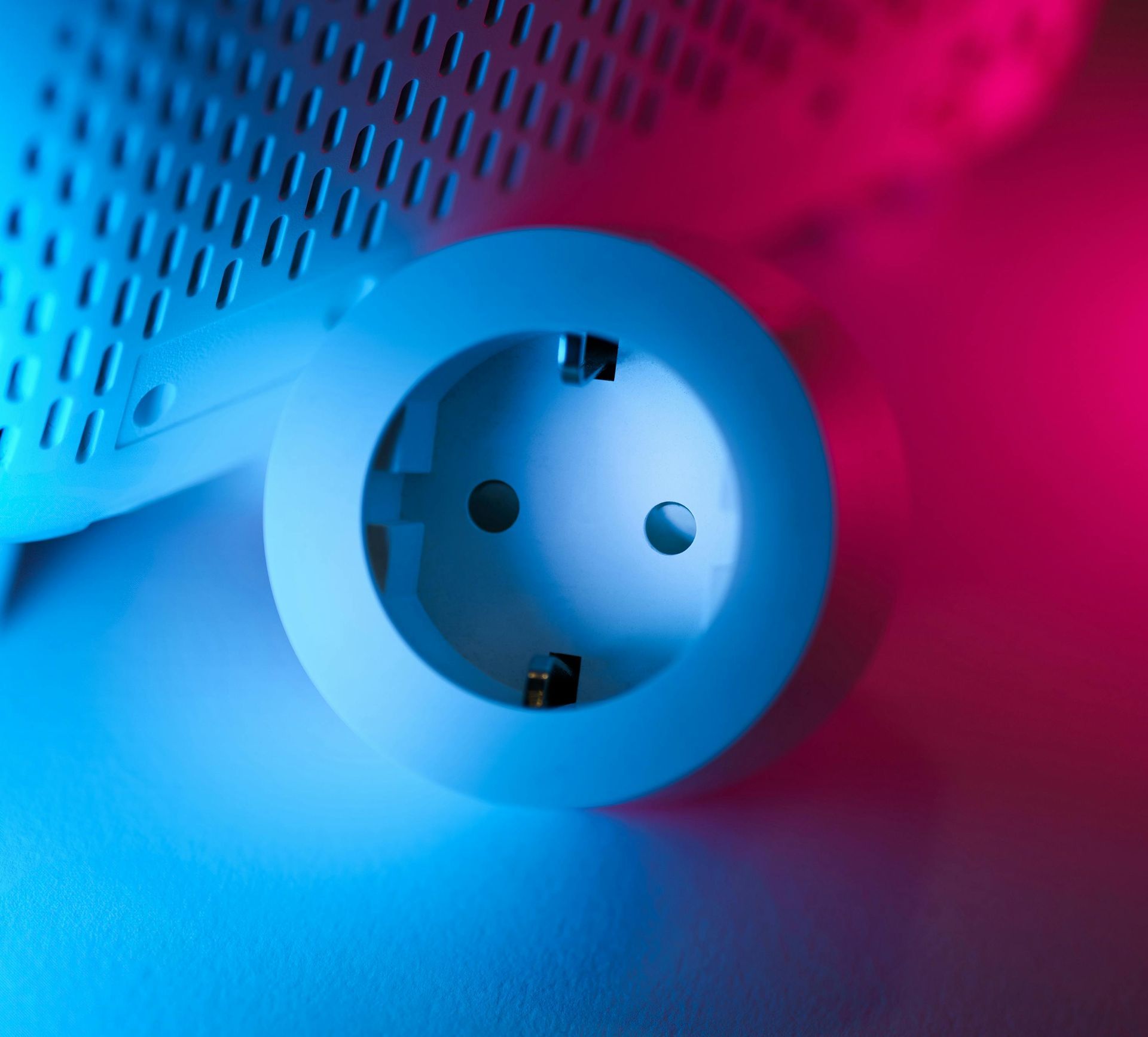 White electrical socket, with two holes and grounding clips, against a blue and pink gradient background.