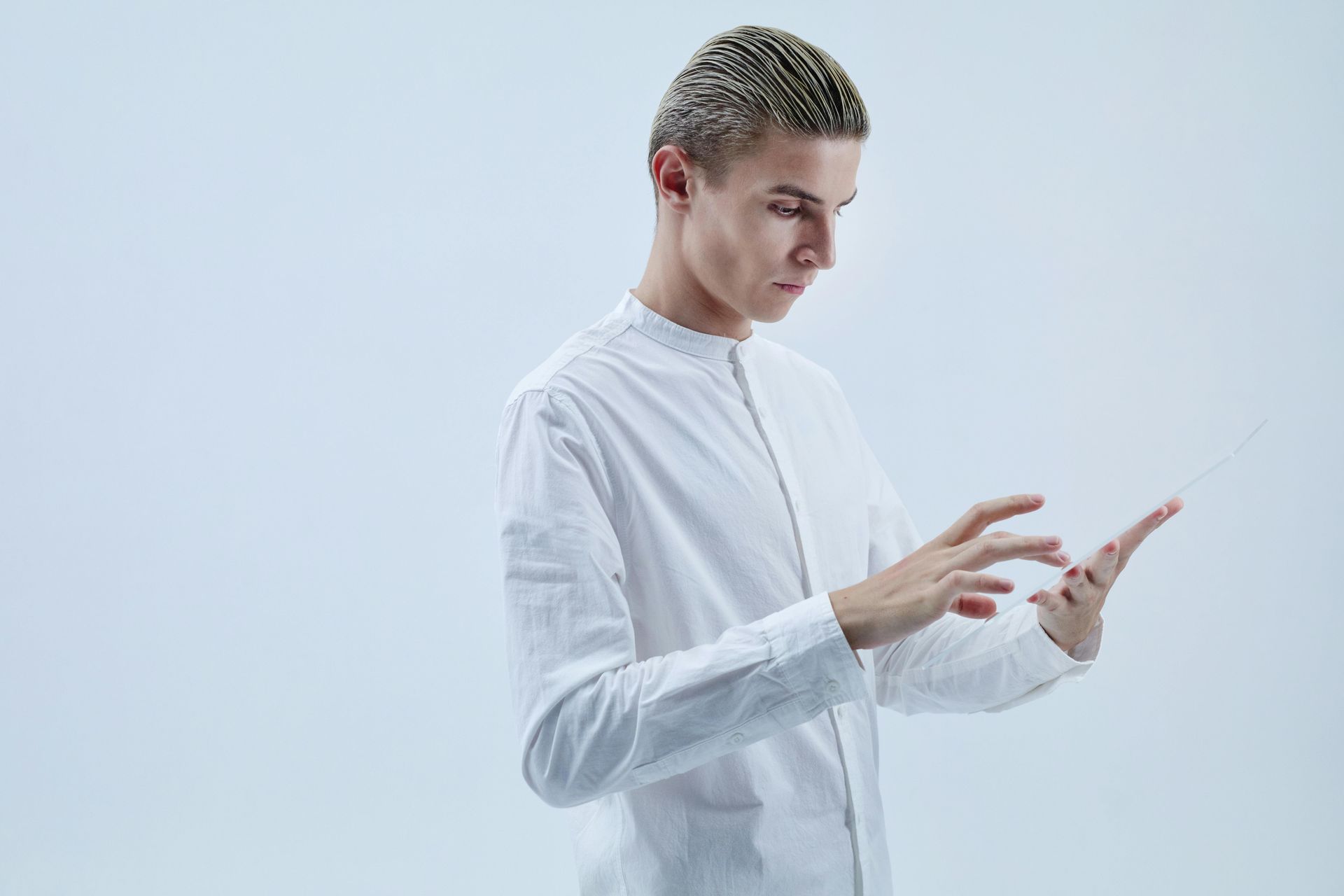 Man in white shirt looking down, gesturing with hands. White background.