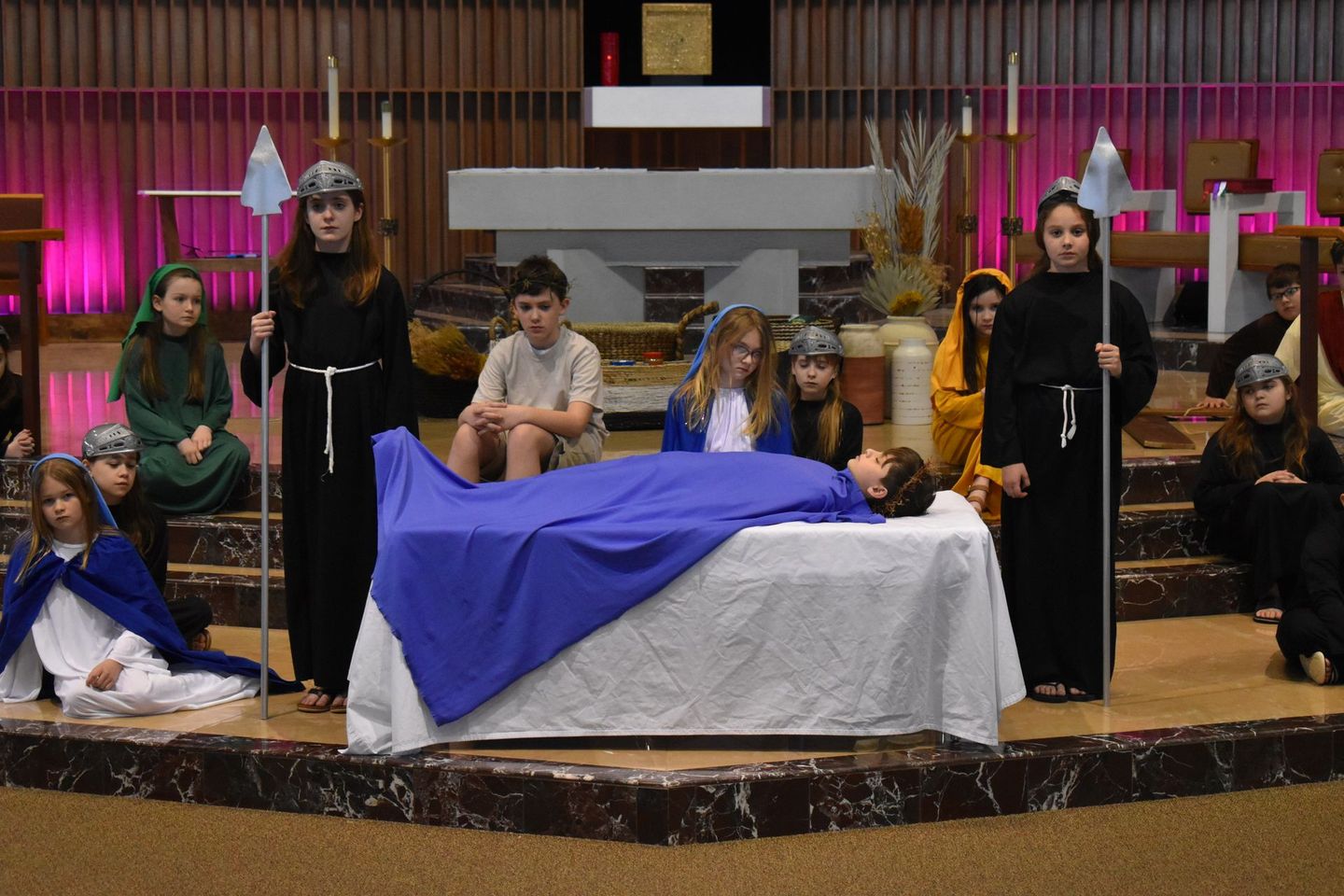 A group of children are standing around a jesus laying on a bed