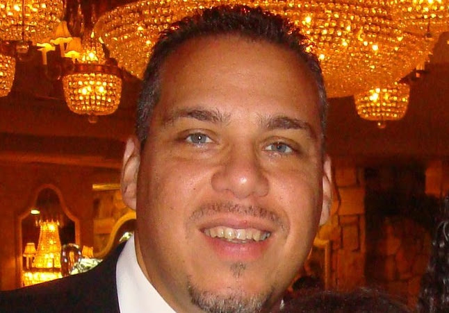 A man in a suit and tie is smiling in front of a chandelier.