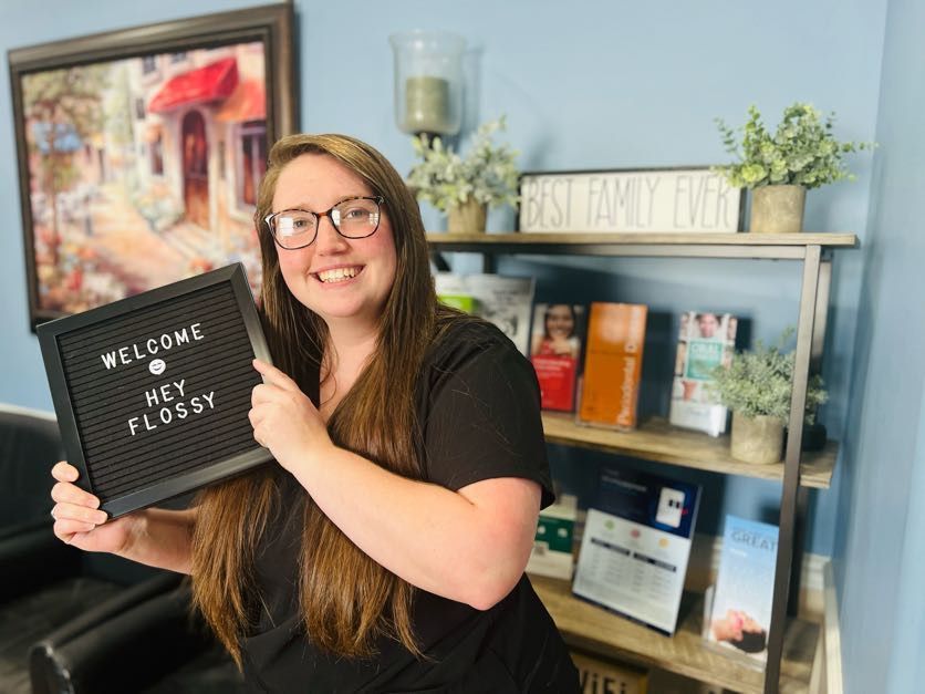 Woman smiling, holding a sign that says