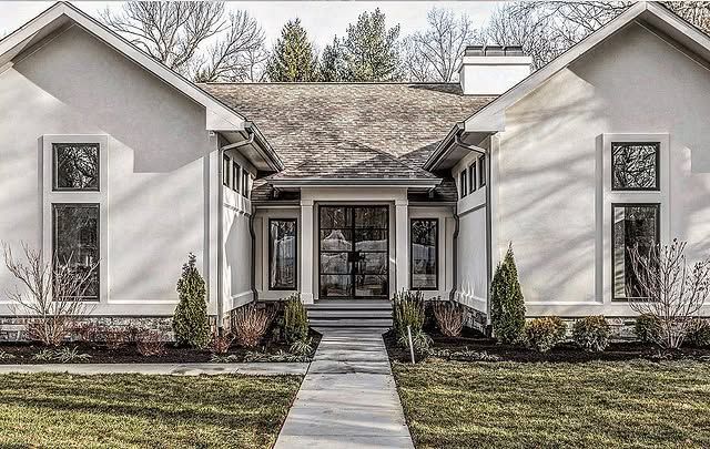White stucco home with dark windows and double doors, a walkway, and green lawn.