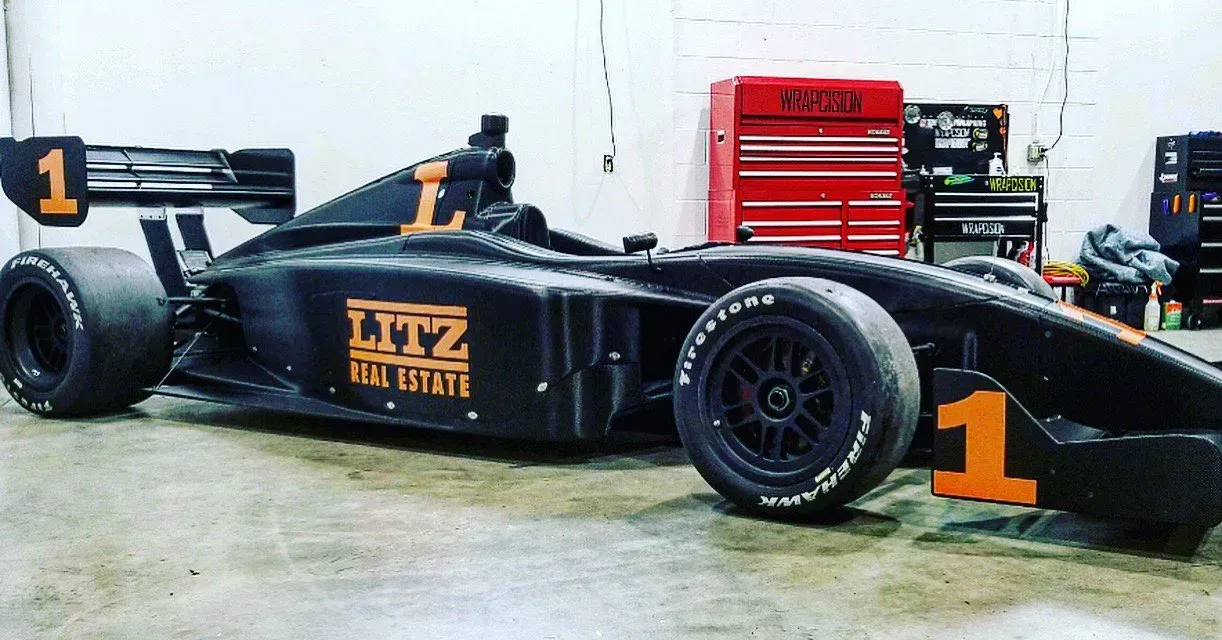 Black race car with orange accents, inside a garage. Number 1 on the side, wing, and front.