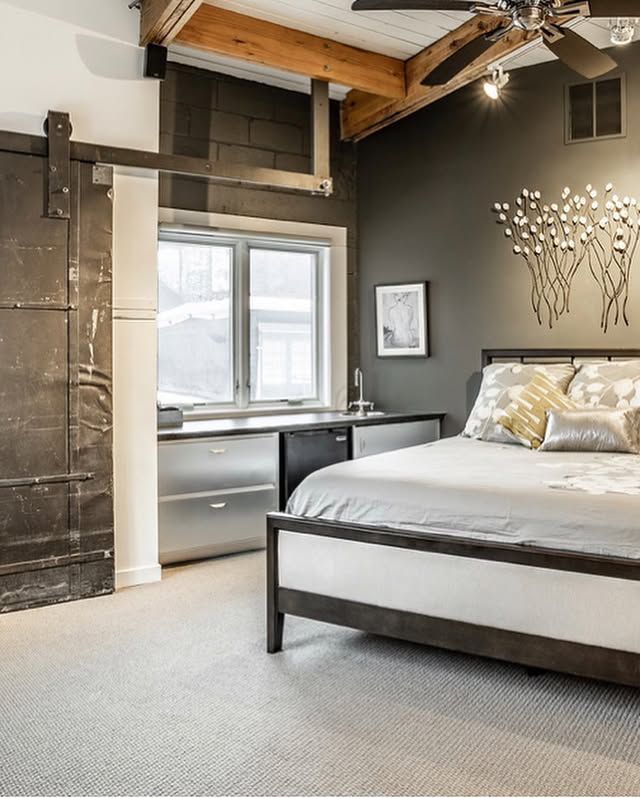 Bedroom with dark gray wall, bed, metallic accents, and sliding door.