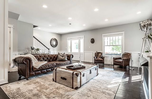 Living room with brown leather sofa, metal trunk coffee table, two armchairs, and large rug.