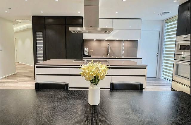 Modern kitchen with white and dark cabinets, a large island, and a vase of flowers on a table.