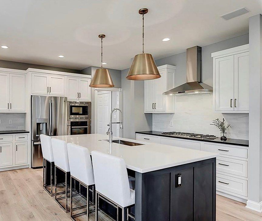 Modern kitchen with white cabinets, black island, gold pendant lights, and white countertops.