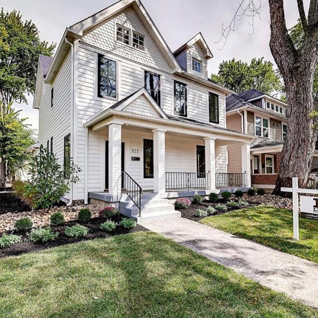 White two-story house with black trim and front porch; green lawn and garden beds in front.