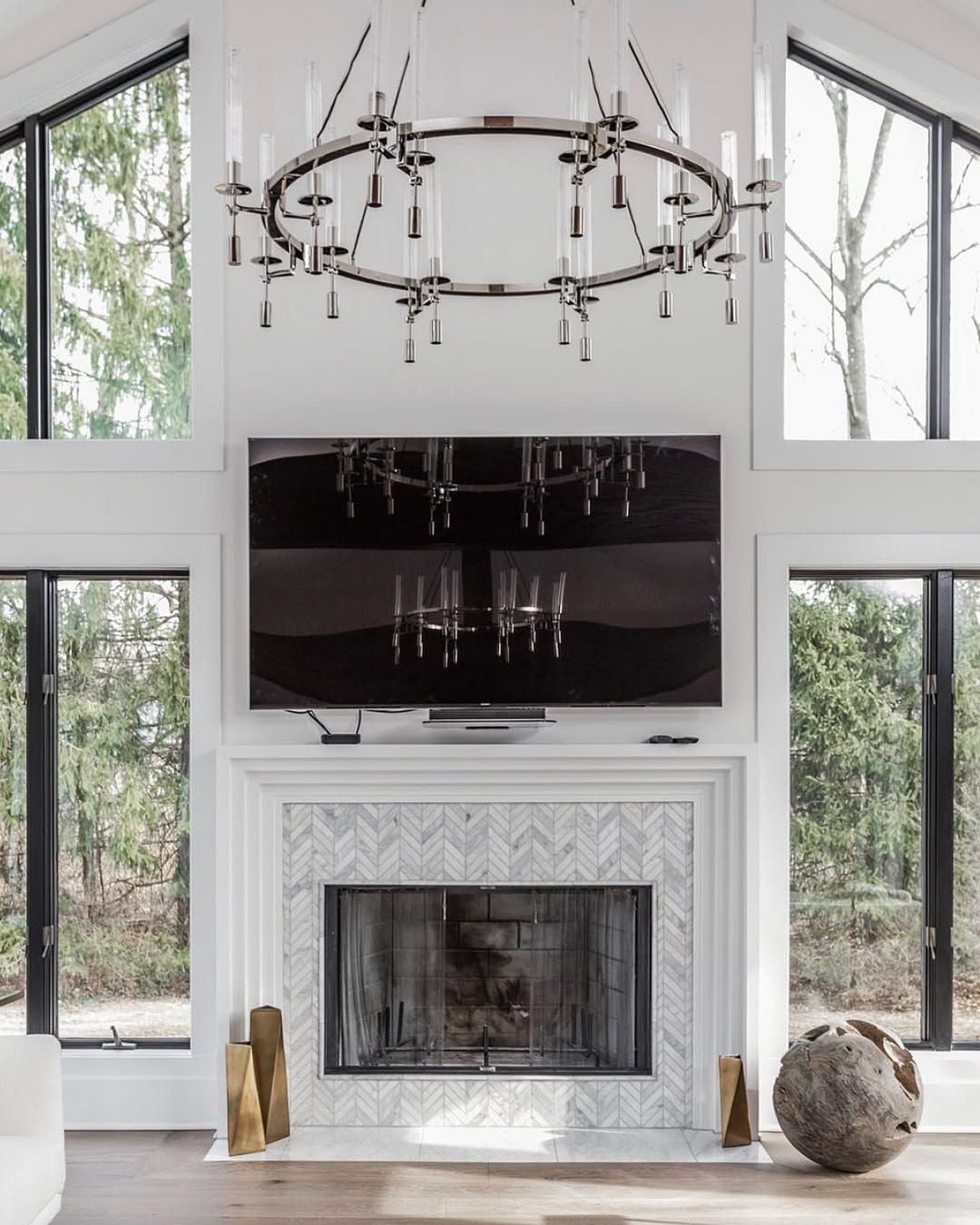 Living room with fireplace, TV, and large windows, featuring a chandelier and decorative accents.