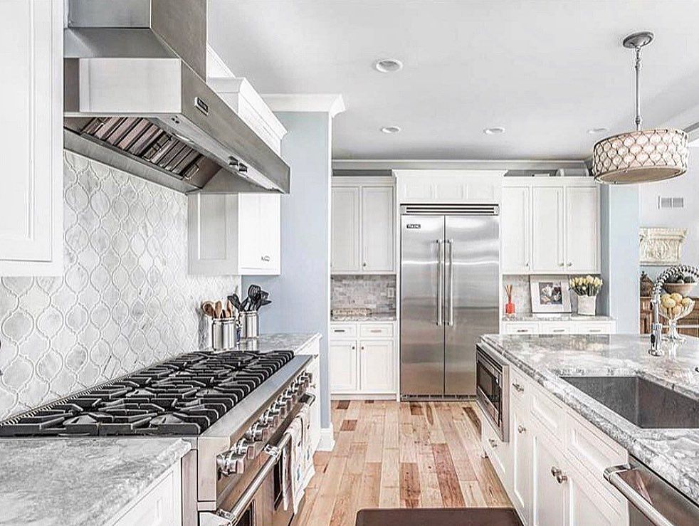 Modern kitchen with white cabinets, stainless steel appliances, and light wood floors.