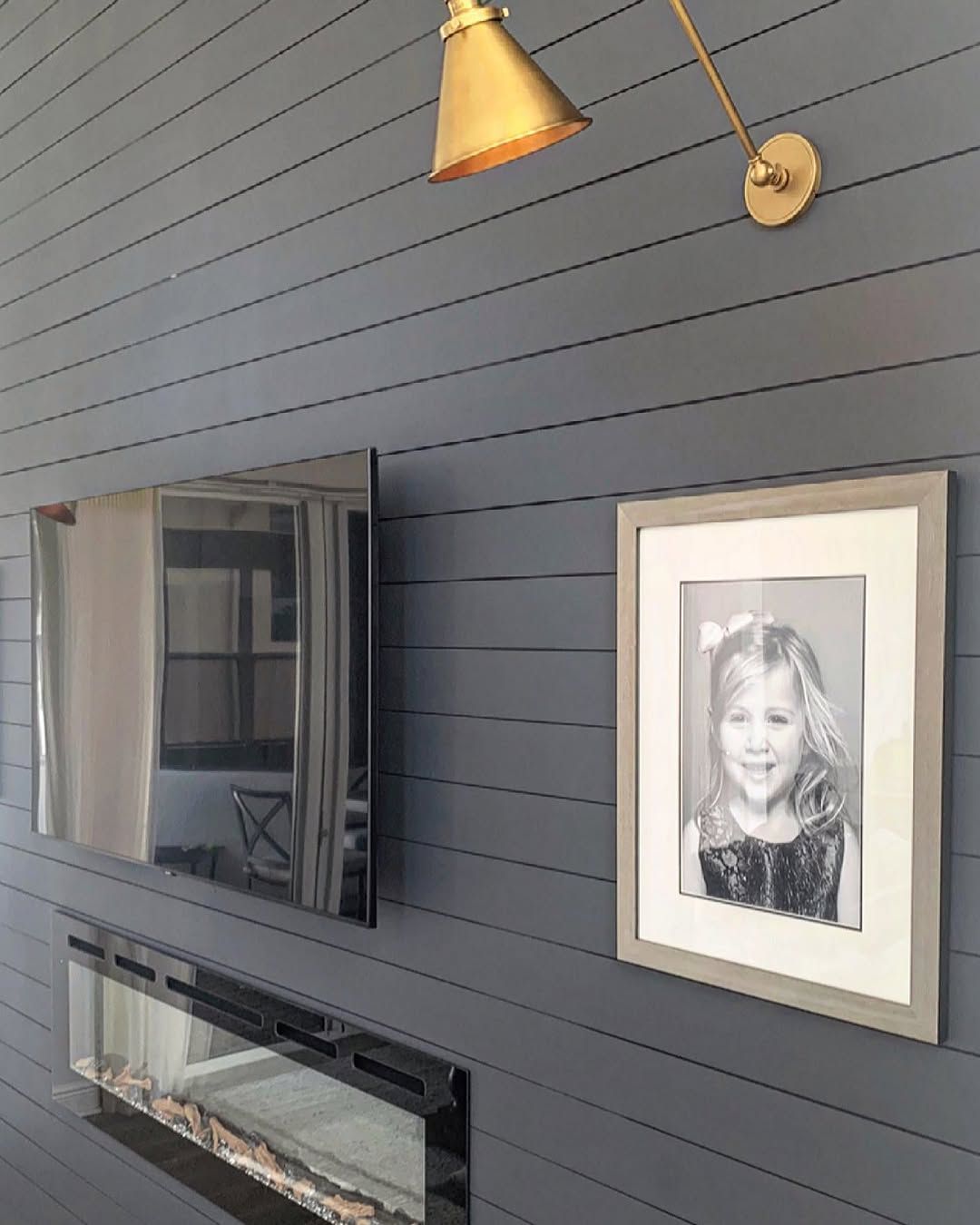 Dark blue plank wall with a gold light, mirror, framed photo of a girl, and fireplace.
