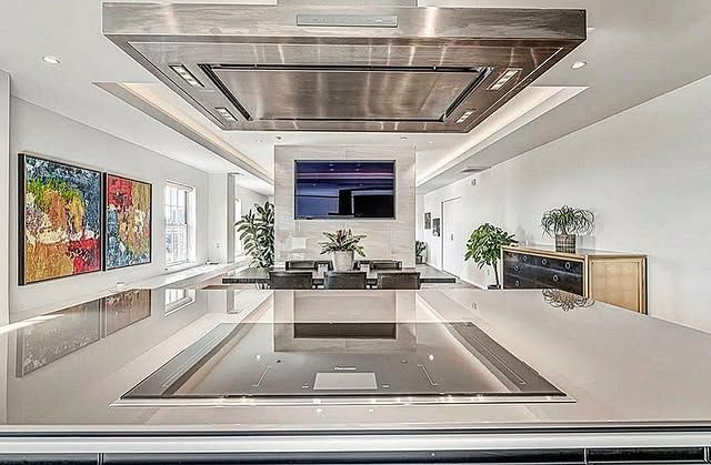 Modern kitchen with a large island, stainless steel range hood, and dining area with a TV.