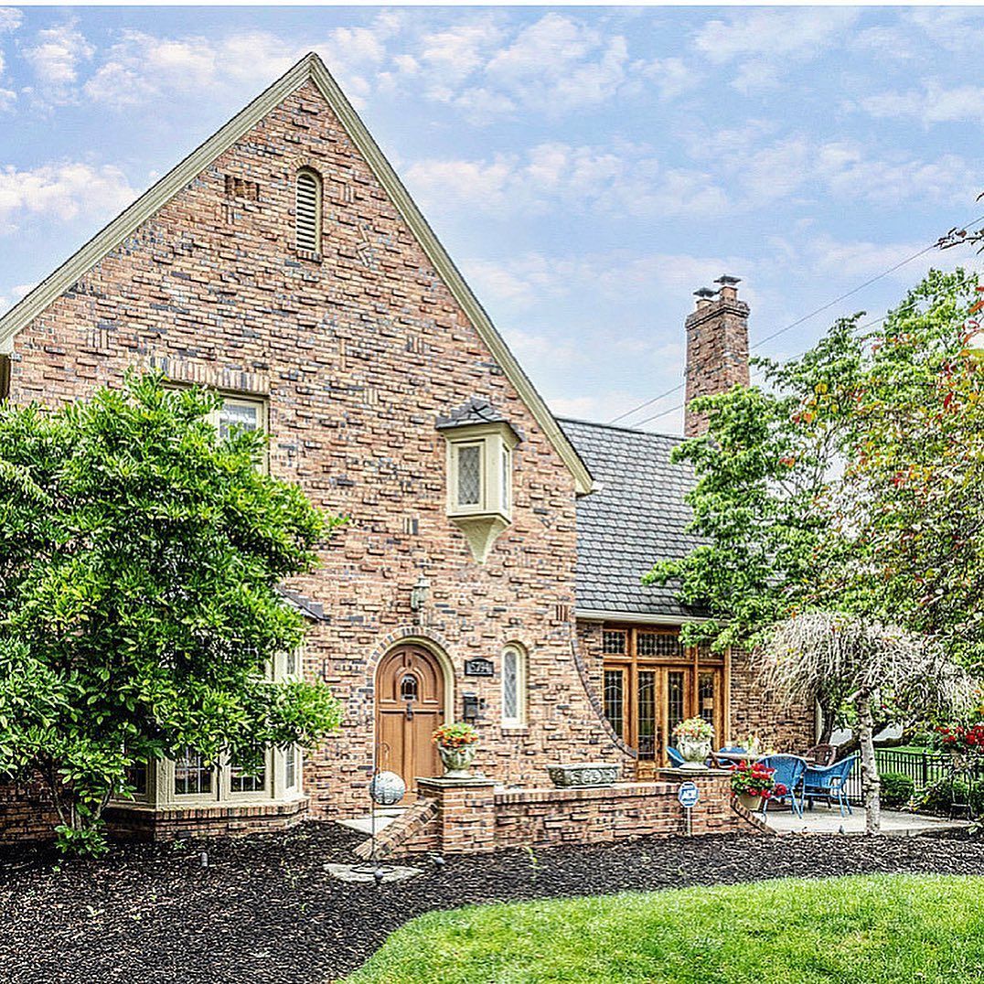 Brick house with a high-pitched roof, arched wooden door, and a lush green lawn on a sunny day.