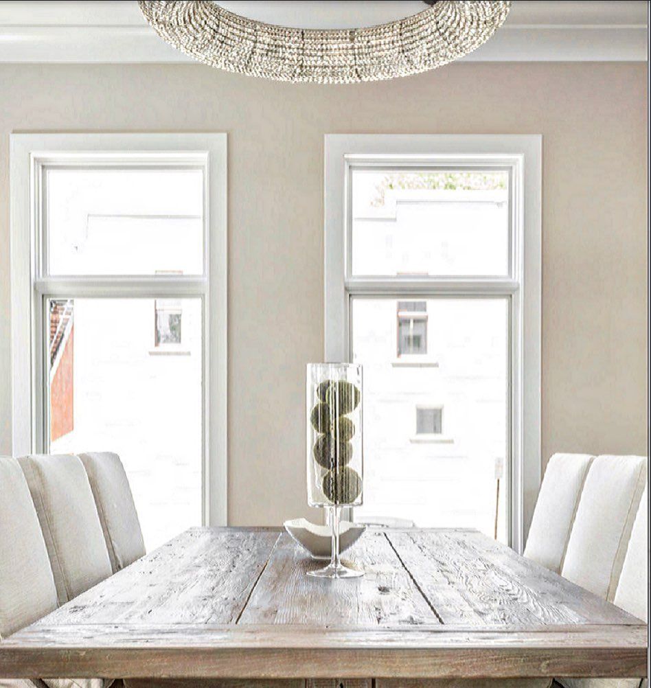 Dining room with wooden table, two windows, white chairs, and a beaded chandelier.