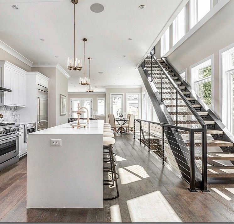 Modern kitchen with a white island, dark wood floor, and a staircase.