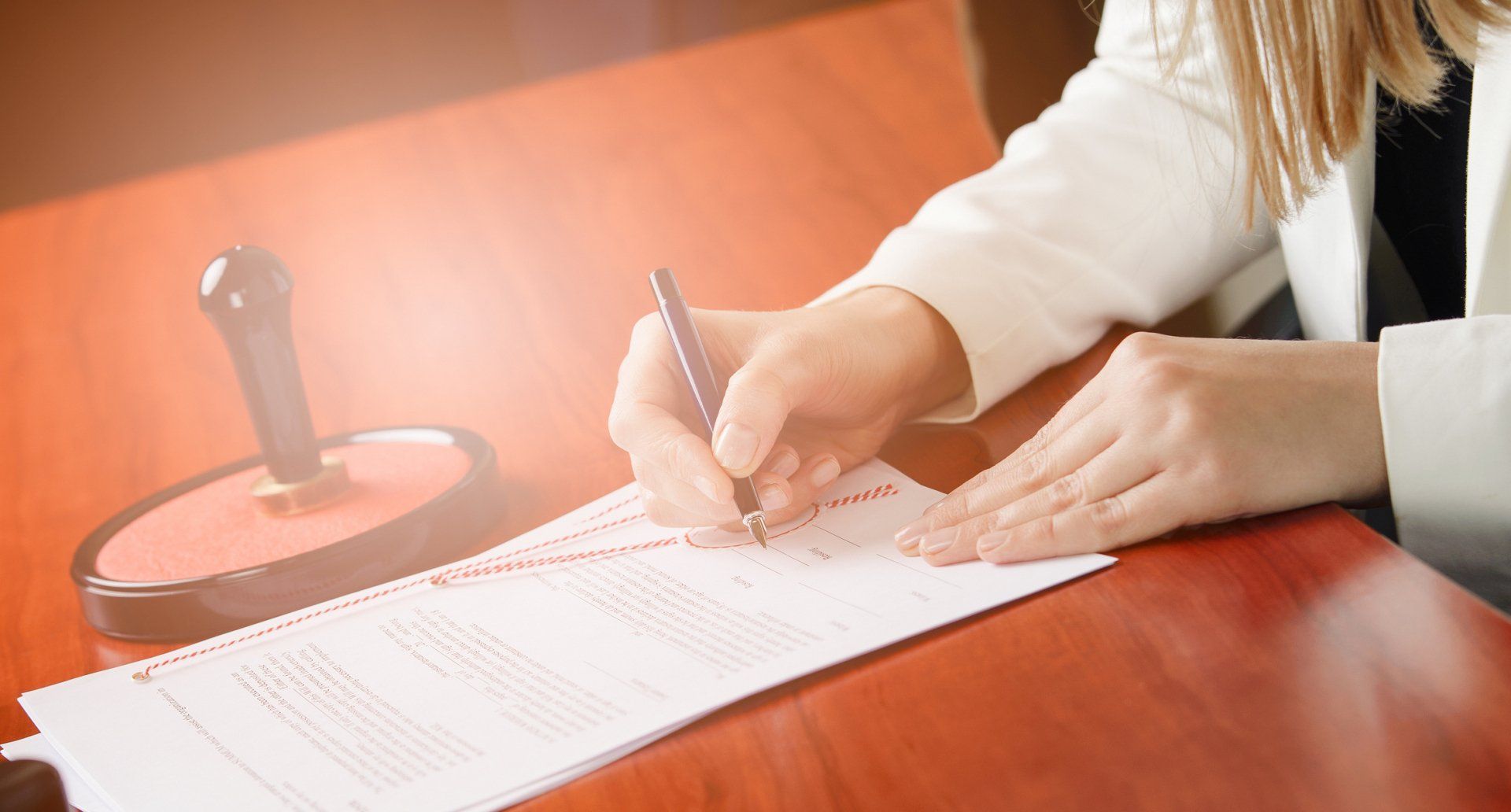 A woman is sitting at a table signing a document with a pen.