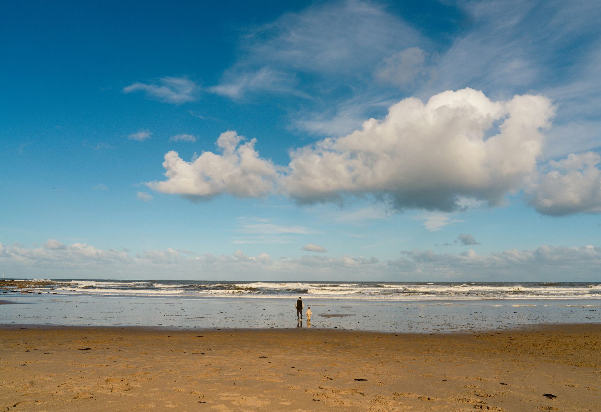A person is standing on a beach looking at the ocean.