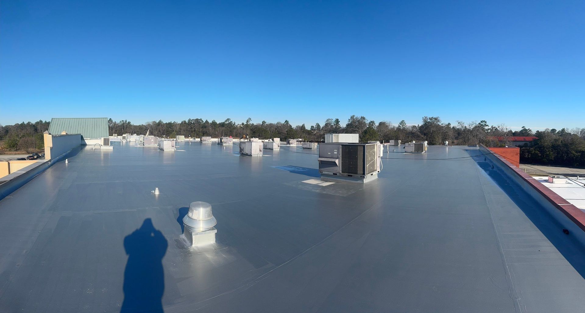 View of a flat commercial roof with multiple HVAC units. Clear blue sky overhead.