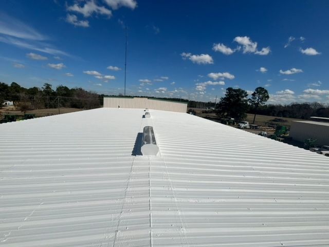 Close-up of a gray metal roof with matching gutters. Black fasteners and vents are visible.