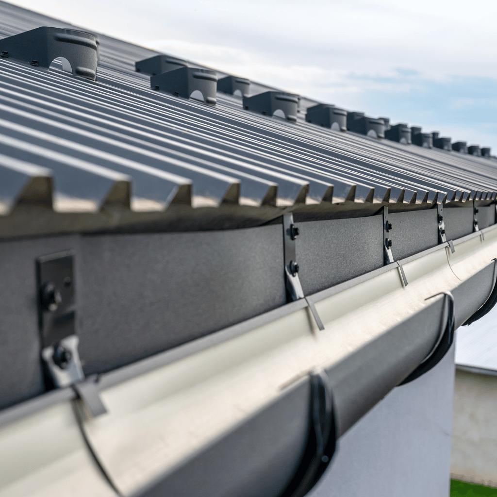 Close-up of a gray metal roof with matching gutters. Black fasteners and vents are visible.