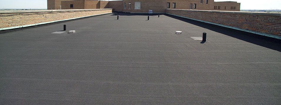 Roofers in blue shirts and hard hats repairing a roof at sunset.