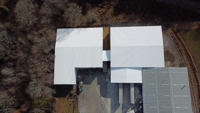 Aerial view of a large white building with a flat roof, surrounded by trees and pavement.