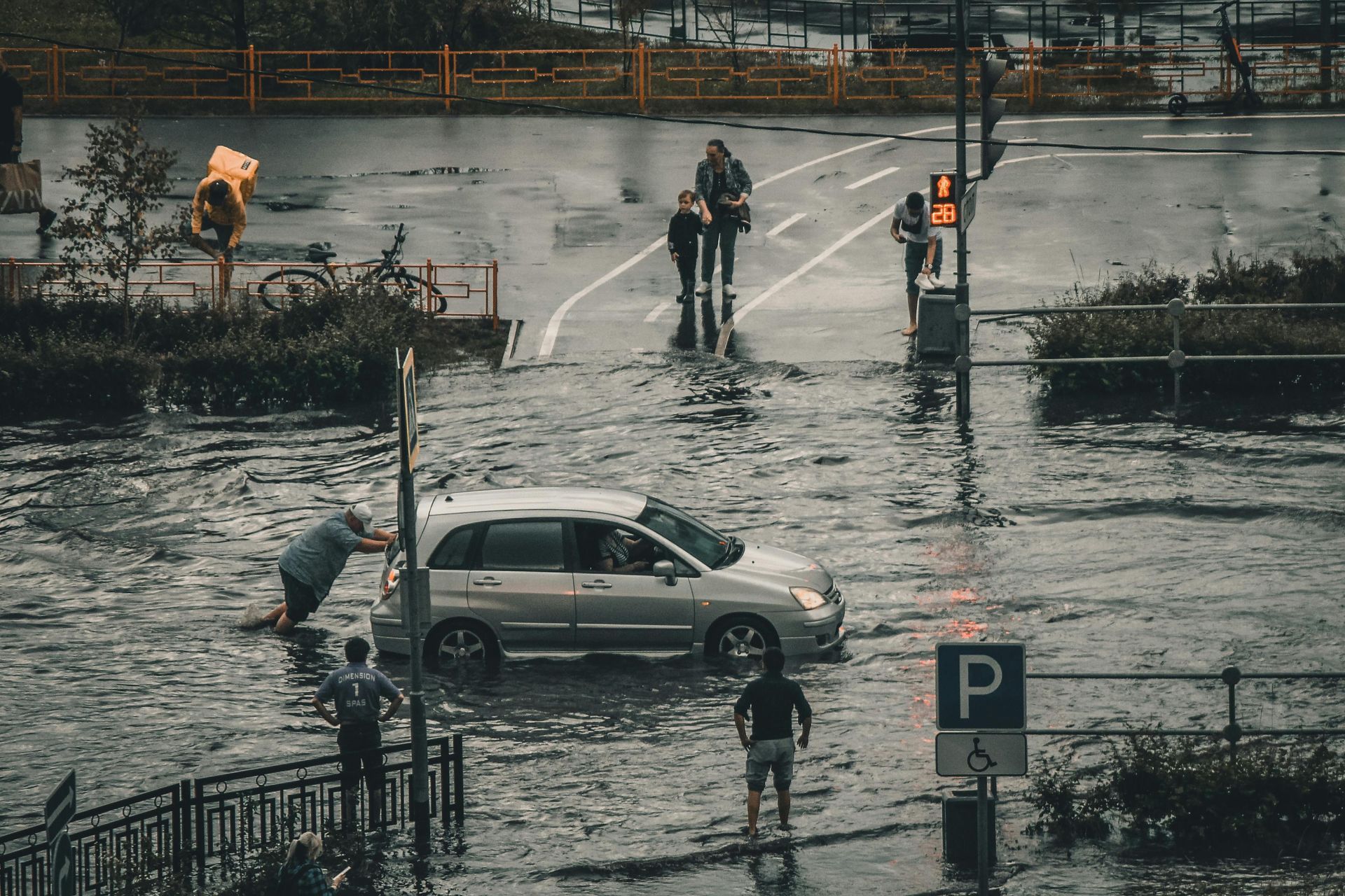 Flooded street with people, a car being pushed, pedestrians wading.