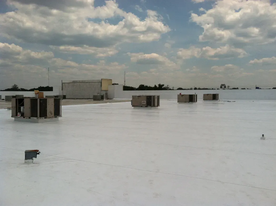 White commercial flat roof with HVAC units, cloudy sky.