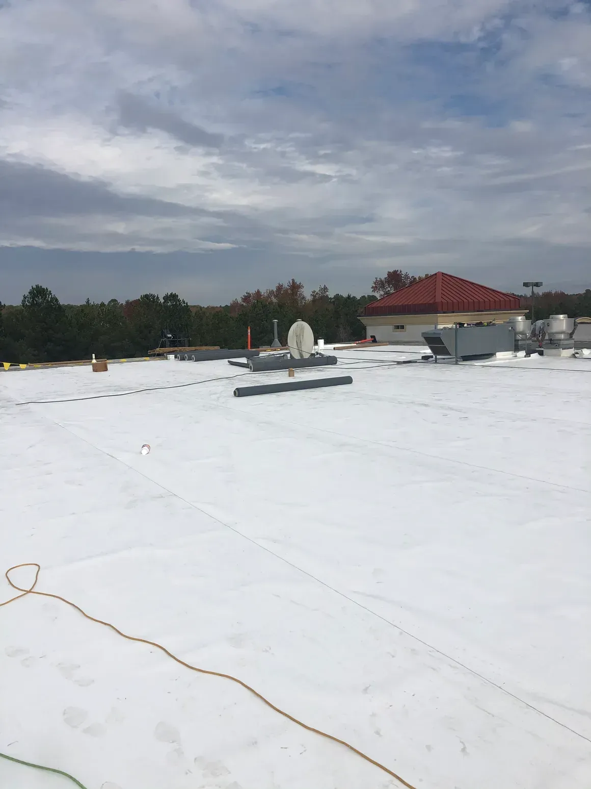 White flat commercial roof with equipment and a red-roofed building in the background. Cloudy sky.