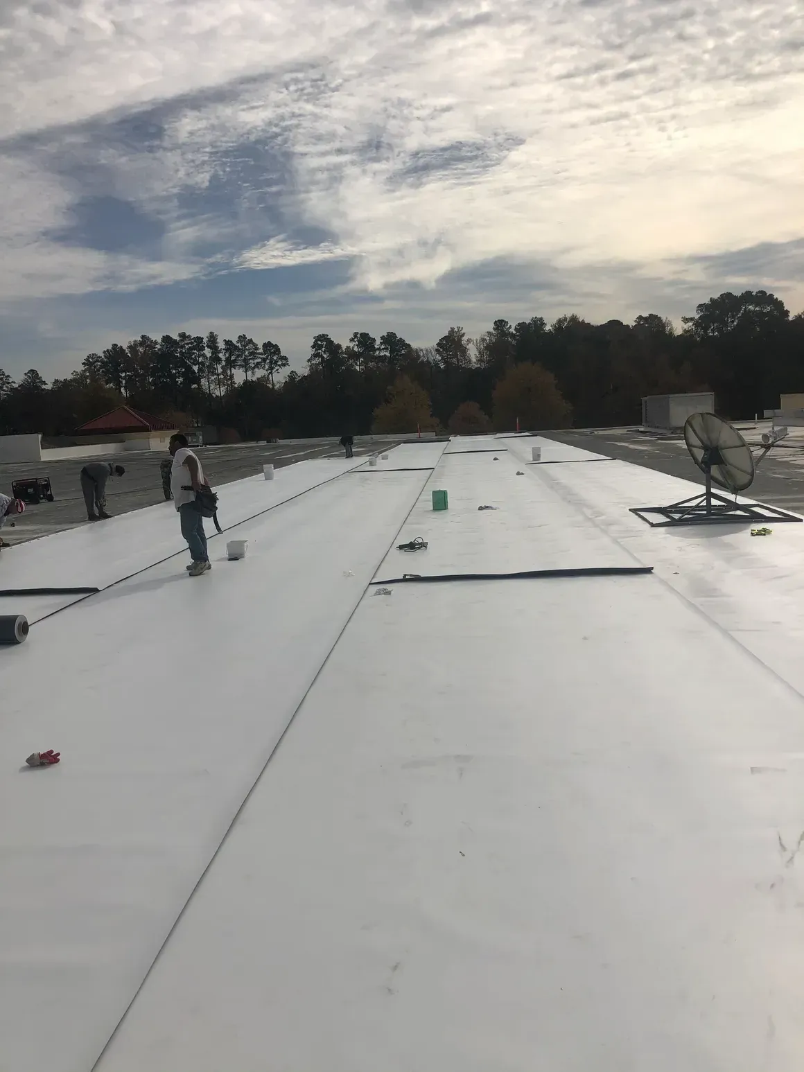 A person working on a white flat roof under a cloudy sky.
