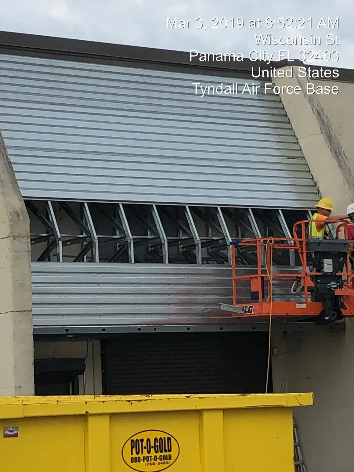 Construction workers on lift near roll-up door at Tyndall Air Force Base, Panama City, FL, with yellow dumpster.