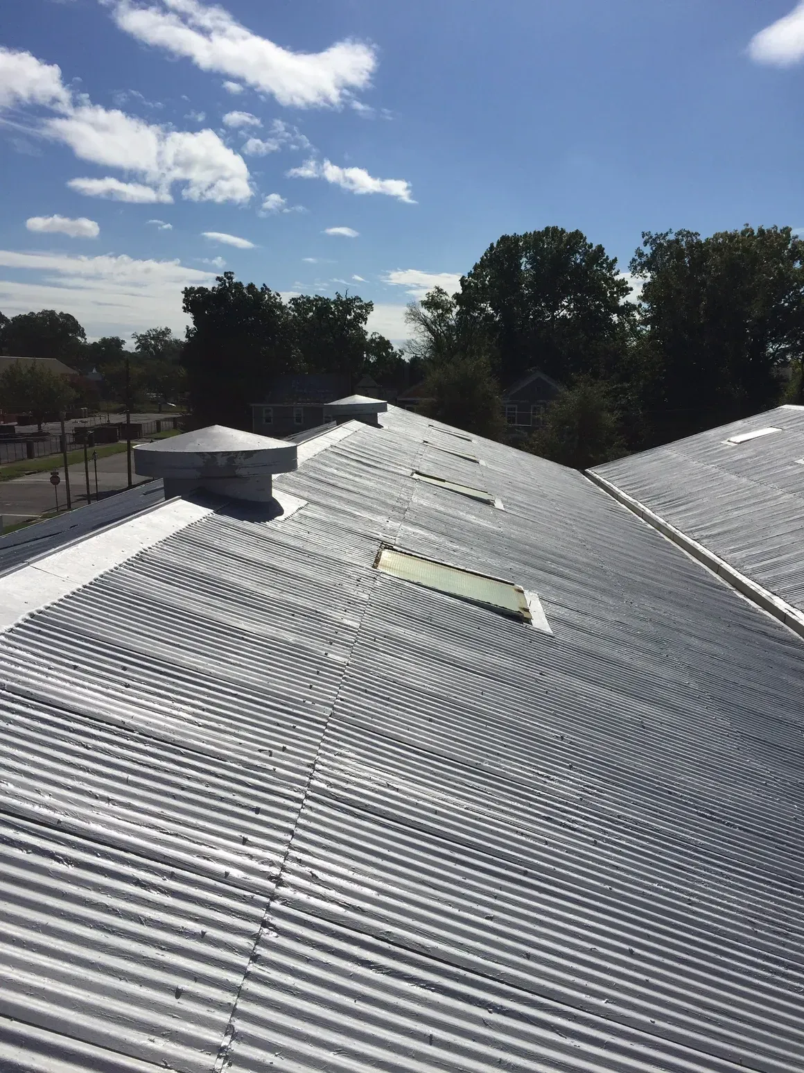 Silver corrugated metal roof with vents and skylights against a blue sky.