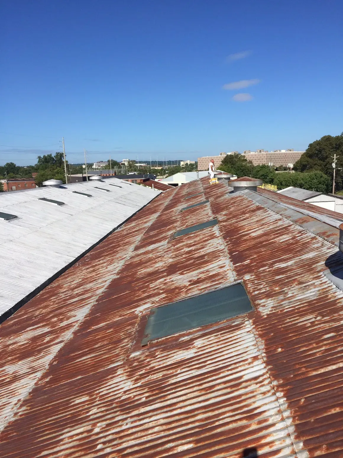 Rusty corrugated metal roof with skylights on a sunny day. Buildings and blue sky in the background.