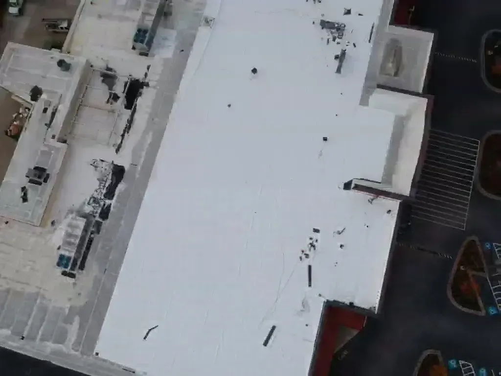 Aerial view of a white commercial roof with HVAC units. Dark debris and a staircase are visible.