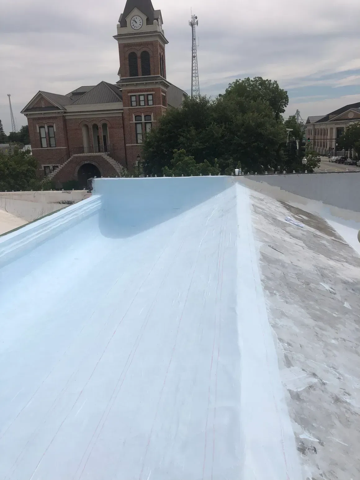 View of a flat roof with light blue coating, town courthouse in background.