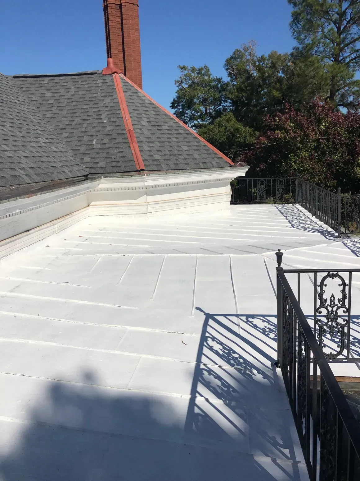 Flat white roof with a black iron railing in the foreground, and part of a roof with a red-topped chimney.