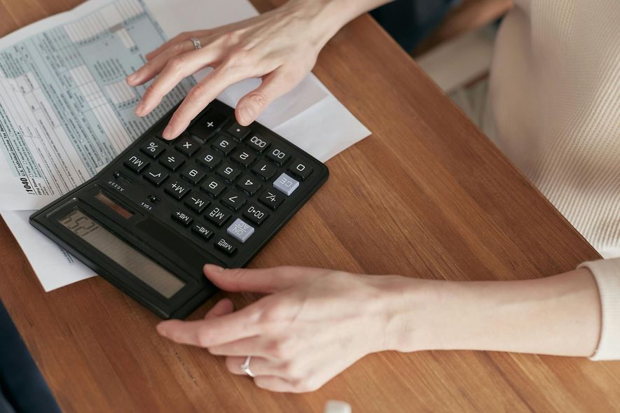 A woman is using a calculator on a wooden table.