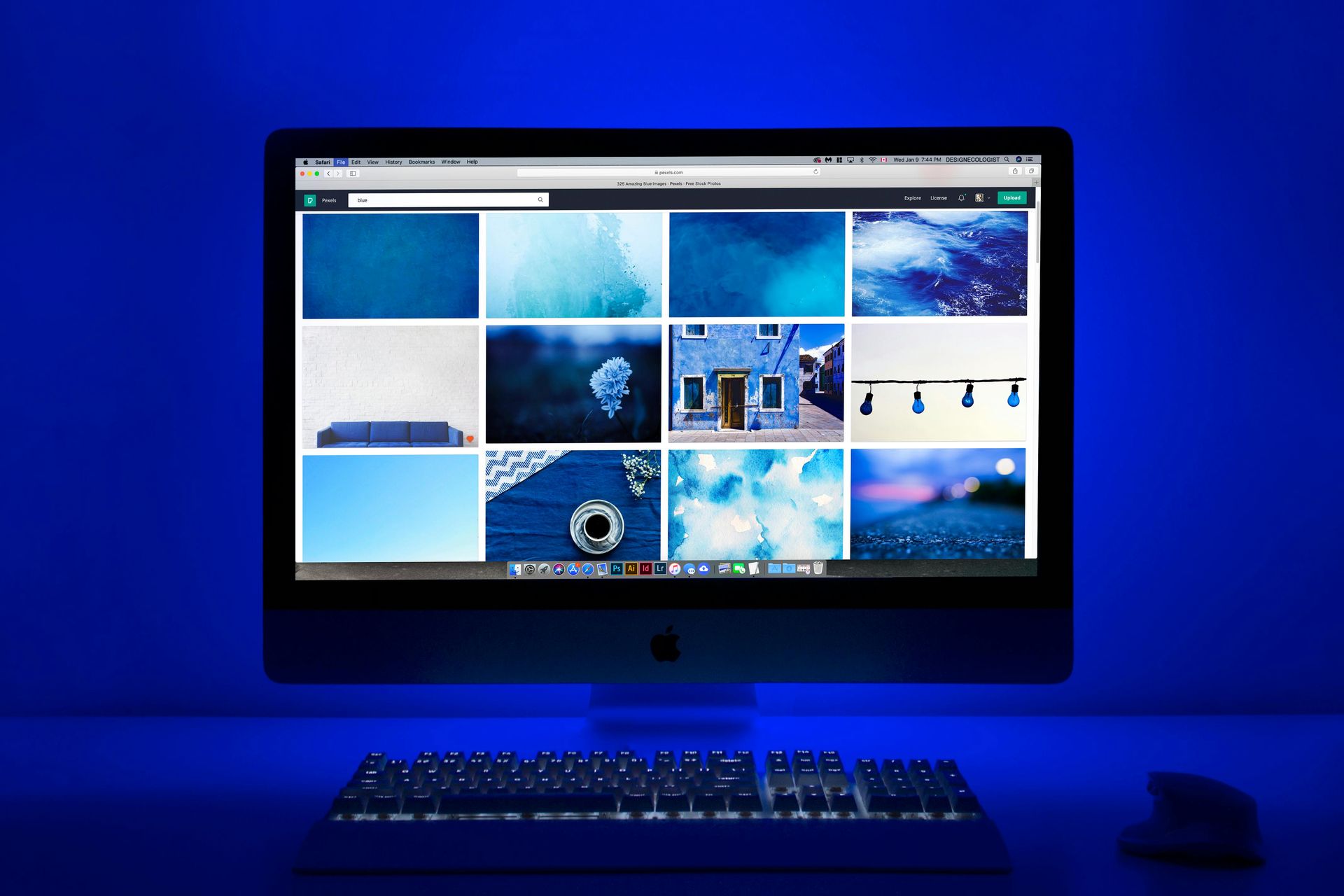 Computer monitor displaying a grid of blue-toned images, with a keyboard and mouse in a blue-lit setting.