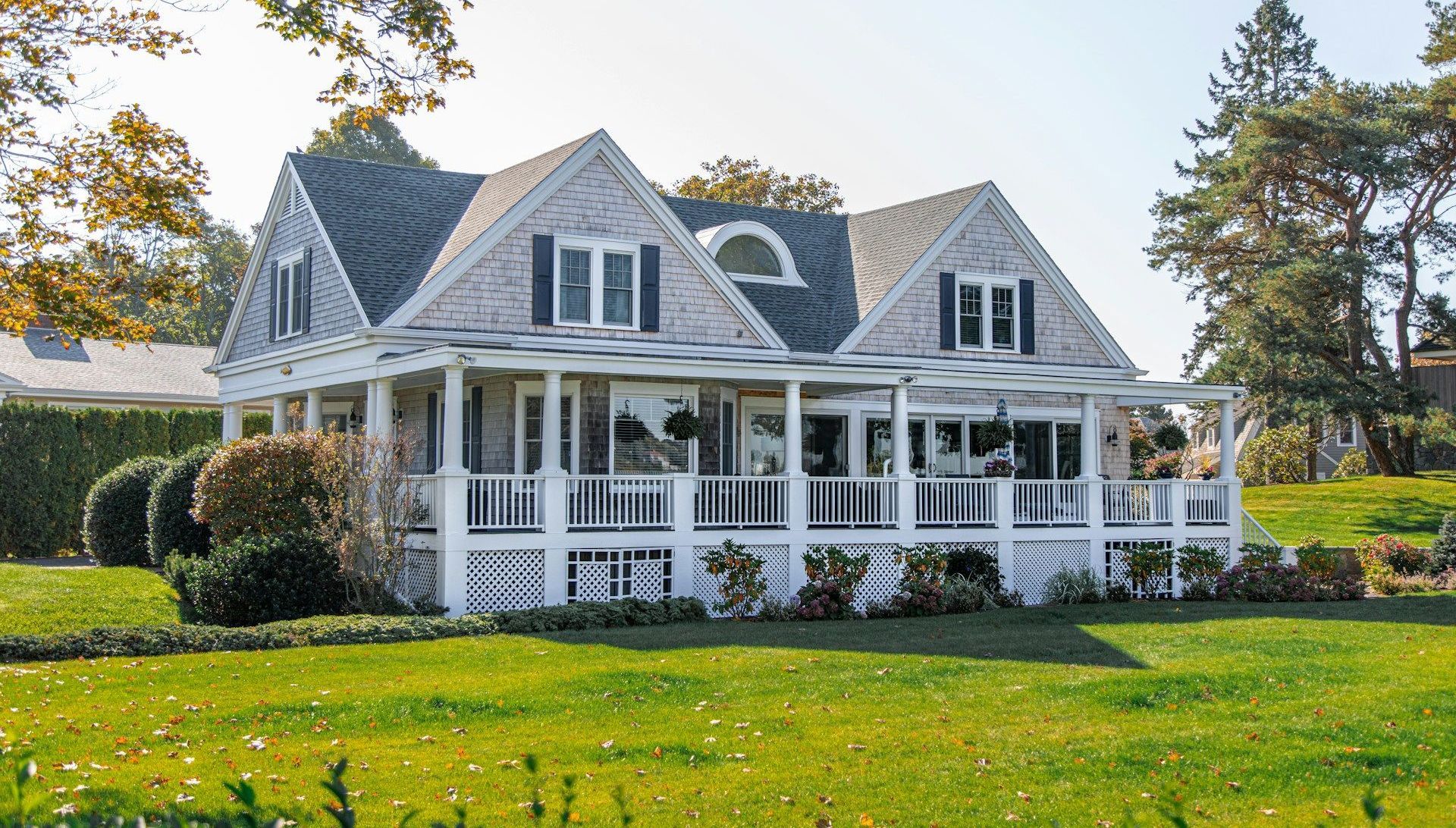 A large white house with a large porch is sitting on top of a lush green field.