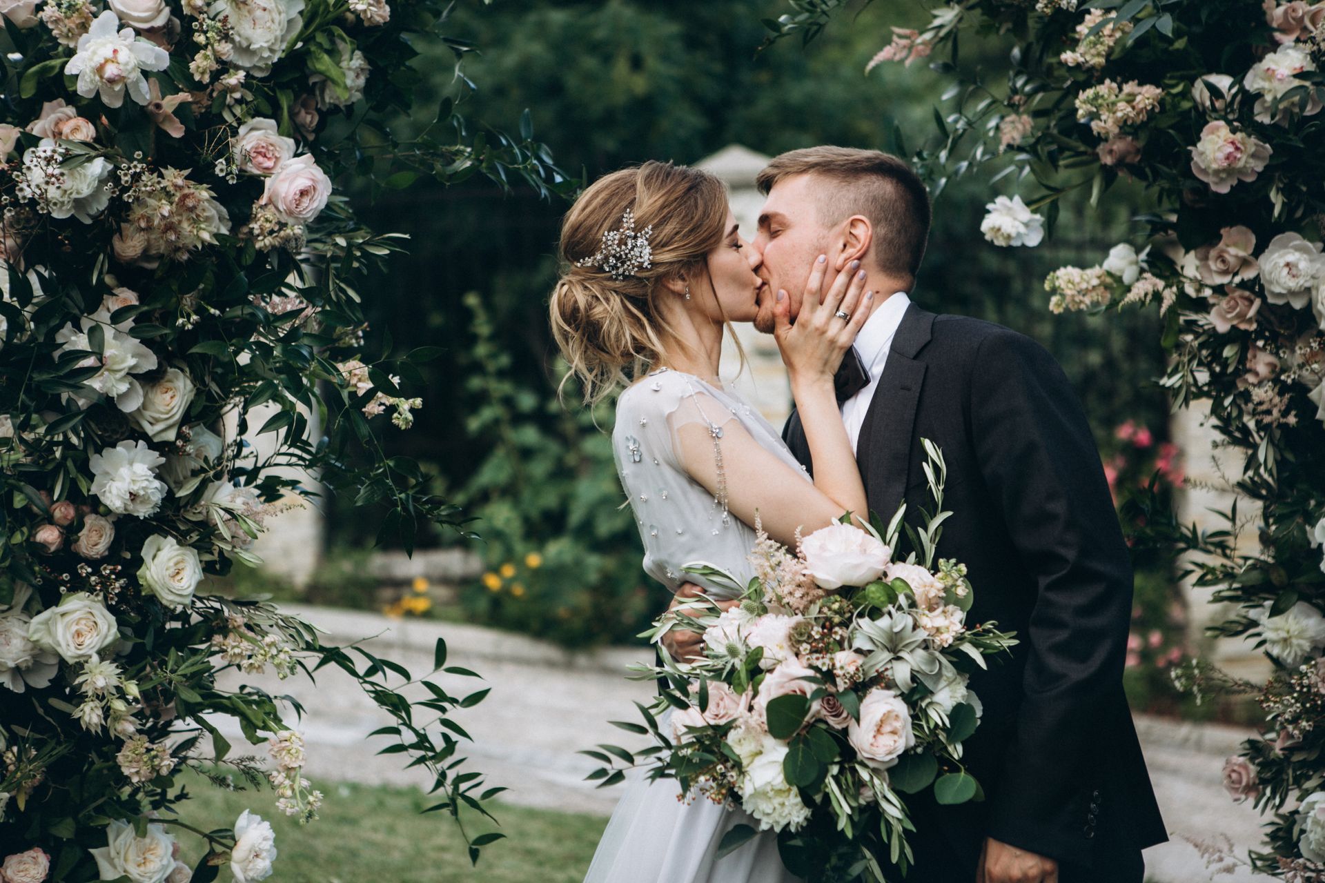 A bride and groom are kissing under a floral arch.
