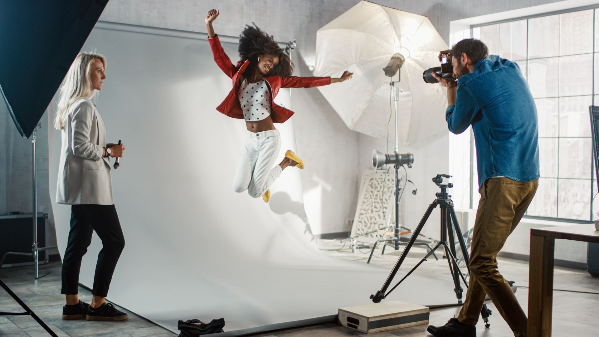 A man is taking a picture of a woman jumping in the air in a photo studio.