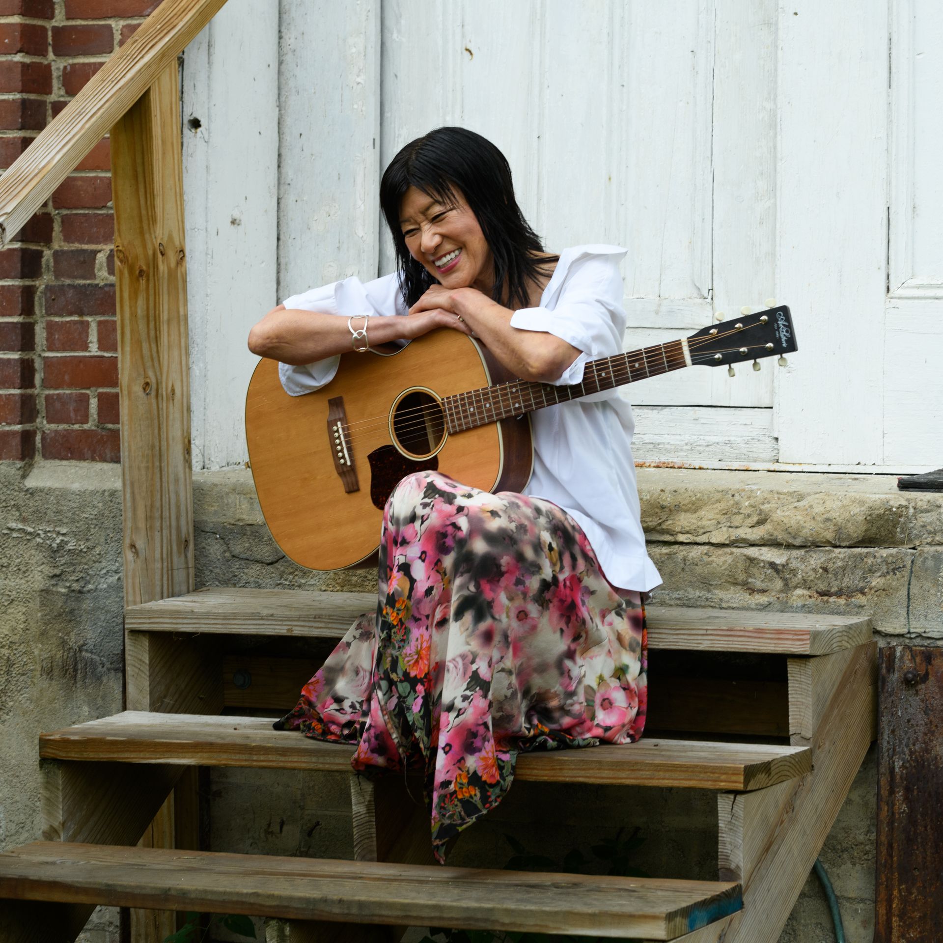 A woman sits on a set of stairs holding a guitar