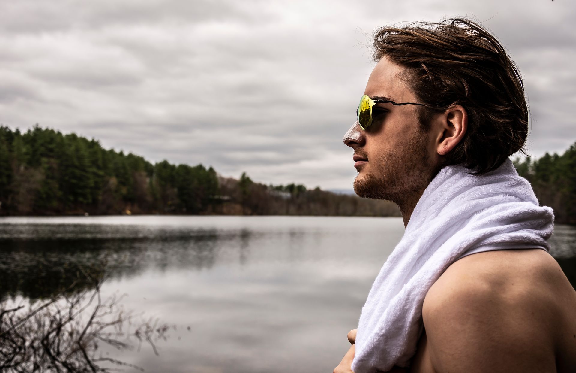 A shirtless man with a towel around his neck is standing next to a lake.