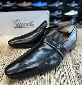 A pair of black gucci shoes are sitting on a wooden table.