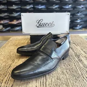 A pair of black gucci shoes are sitting on a wooden table.